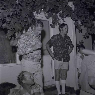 Two men in casual clothes addressing an audience at a private home.