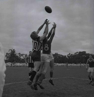 Two footballers jumping to reach a ball.