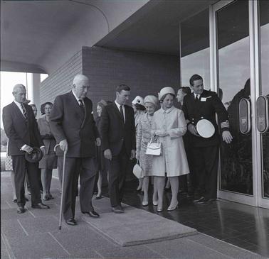 A gathering of around ten people in suits and coats at a doorway of a business establishment.