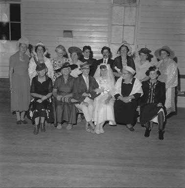 Fifteen ladies dressed in performance costume posing for a photograph in two rows.