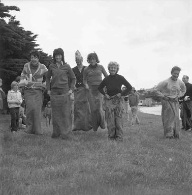 Eight adults and childdren racing in a sack race,