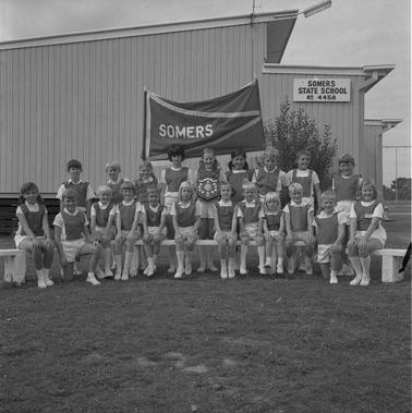 Twenty one sdchool children in sports clothing holding an honour plaque posing for a photo in two rows outside Somers Primary School.