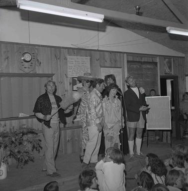 Six people in costumes performing on a stage in front of an audience.