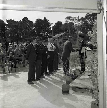 A C.F.A. official shaking hands with a man in front of an audience of many people with five men standing in a line in front of the crowd.