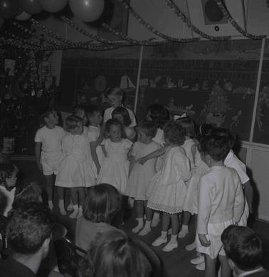 Eleven young girls and boys dressed in white on a stage in front of an audience