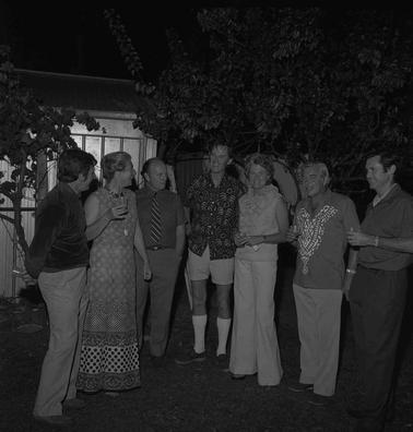 Four men and two women standing outdoors in a semi circle posed for a photograph.  It is night time,