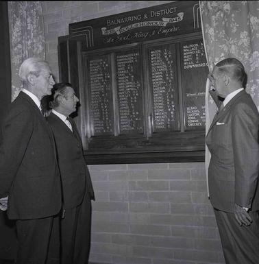 Three men looking at an unveiled Honour Board.