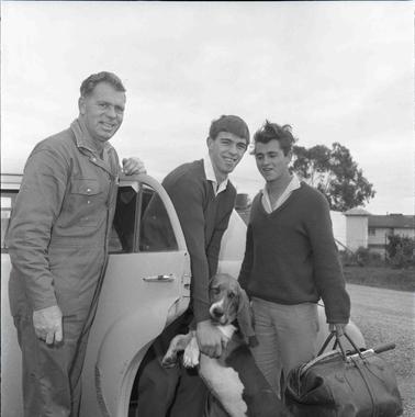Three men at a car’s open door | one is carrying luggage.