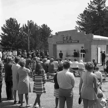 Shoreham CFA with a crowd of people facing three men in uniform one of whom is on a dias talking into a microphone.