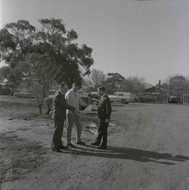 Three men outdoors inspecting a document.