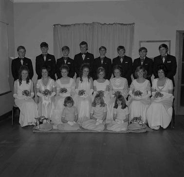 Ten young couples in formal attire, all girls wearing white ball gowns and four younger girls posing for the photograph in three rows.