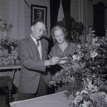 A male and a female figure appraising a flower arrangement.