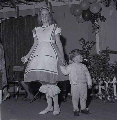An adolescent girl dressed in Alice in 
Wopnderland costume holding a young boy’s hano date.