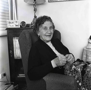 A woman sitting in an arm chair near a window  crocheting a rug