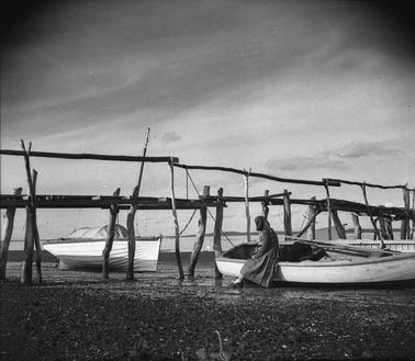 A rustic fishermen’s jetty with two boats and a female figure.