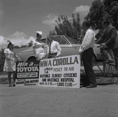 Two men and two women at signs promoting a car raffle.