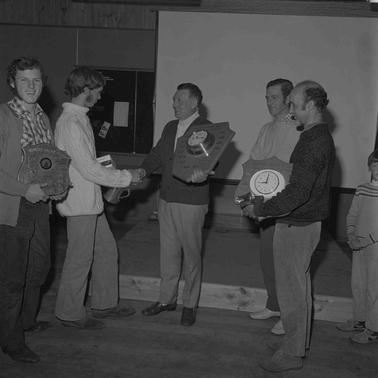 Five men in casual clothes.  A presentation of clocks as prizes to the two young men at left.