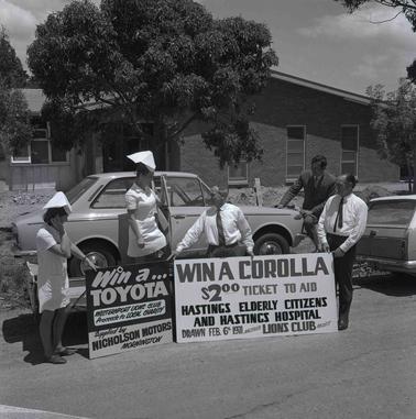 Two men and two women at signs promoting a car raffle.
