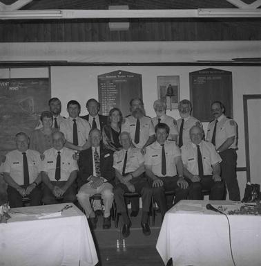 Thirteen men and two women in two rows, front one seated, inside Somers Yacht Club at two white cloth covered tables.  An honour board is on a wall behino date.