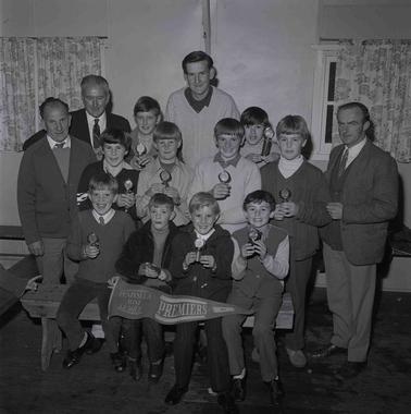 Ten young boys and four adult men posing for a photo in three rows.  Boys in the front row are holding a pennant.