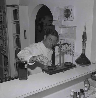 A man dressed in a lab coat weighing powder on balance scales.