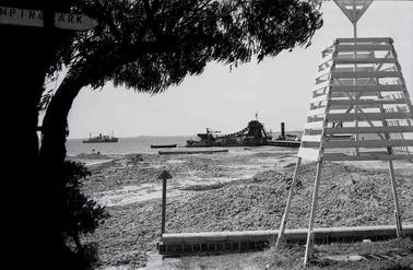 A jetty with a dredge behind a navigation marker on the shore