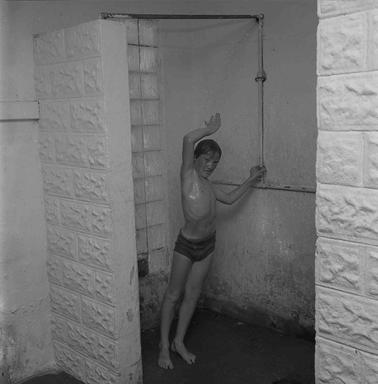 Indoor view of a public shower room with a boy under a shower.