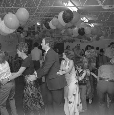 Adults and children holding each other’s backs in a ‘conga line’ ata festive function.