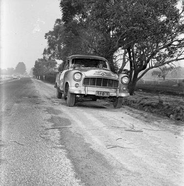 A car on an unsealed road with trees on one side.