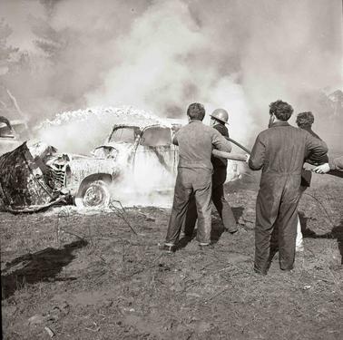 Four men pointing a firehose at a burning car.