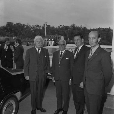 Four men wearing suits posing for the camera outdoors.