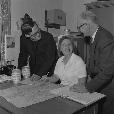A woman in nurse’s uniform talking with two men.