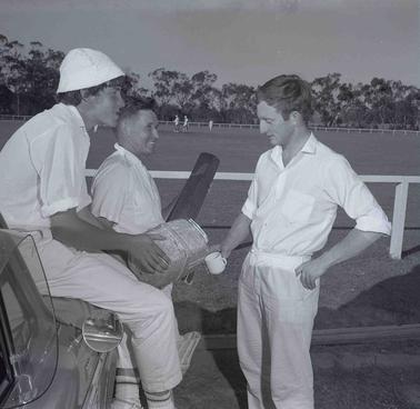 Group of three men in cricket whites, chatting, one is seated.