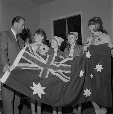 Four girl guides and a suited man all holding an Austraalian flag.