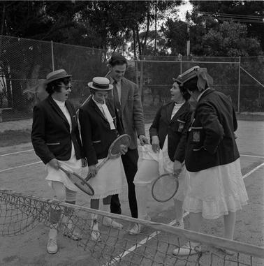 On a tennis court four our women in tennis clothing are talking to a man in coat and tie.