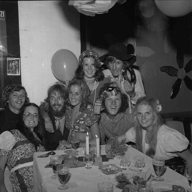 Eight young people in festive dress gathered at the end of a patry table.