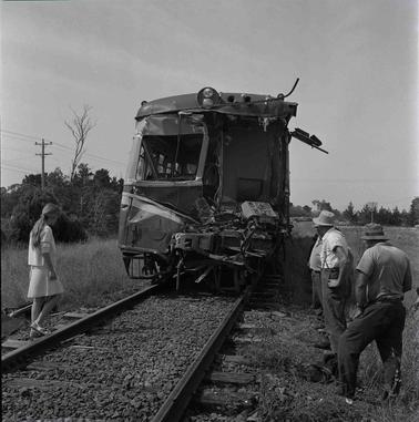 Three men and a girl looking at a damaged train carriage.