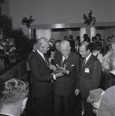 Three men at a formal function inspecting a model of a ship.
