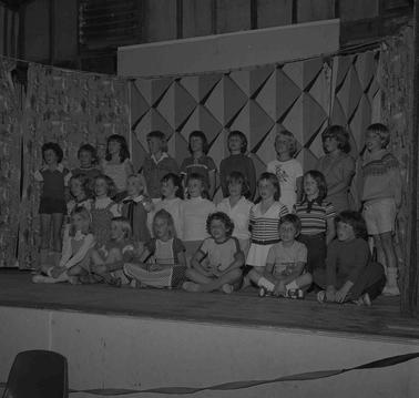 A tableau of thirty children in three rows, sitting, kneeling and standing while singing.