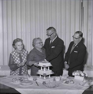 A senior couple behind a celebratory cake with two people looking on