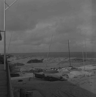 A sandy depression on a beach in front of a building with yacht boats on the sano date.