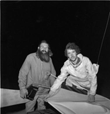 Two men dressed in warm casual clothing attending to a sail.  One older and bearded the orher a young man.