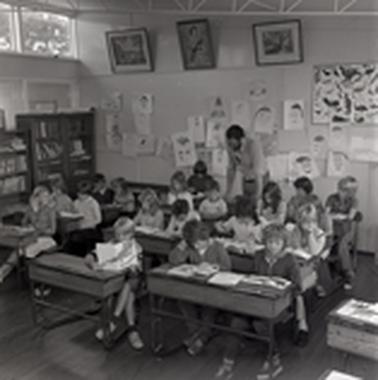 Nieteen children and their teacher at work in a classroom.