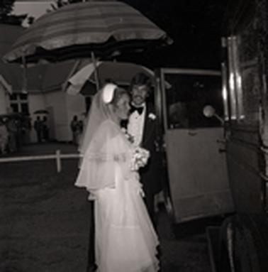 Bridal couple at an open car door.  People and a weatherboard church building ar in the backgrouno date.