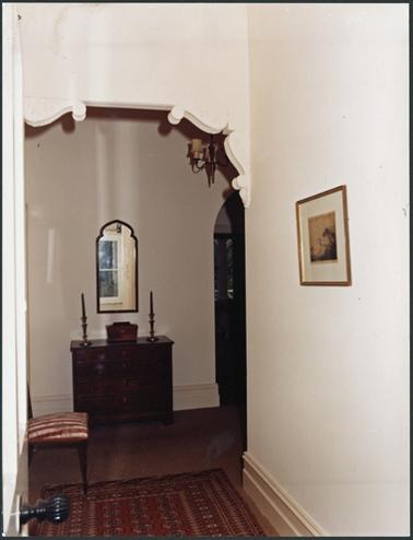 A colour image of the inside of Southdene, featuring the hallway with decorated archway and furniture consisting of a chest of drawers, mirror, candlesticks and framed picture