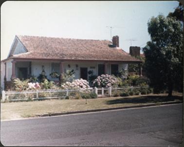 A white weatherboard residence with verandah and one chimney a wire fence divided by gate in
front of the building