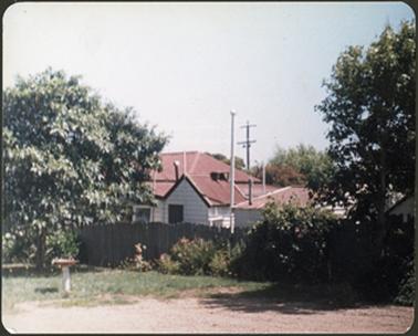 A rear view of a weatherboard residence and outhouses with red iron roof