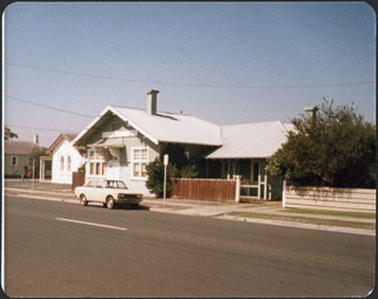 A weather board building with a small verandah over bank entrance and to the right of the building a larger verandah over the side entrance an iron pitched roof with one chimney
