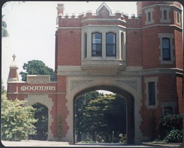 A two storey red brick building with cream stucco detailing, name on left archway, central archway with bay window tower on right