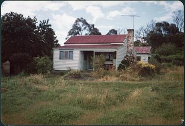 White weather board cottage, red iron roof, chimney, outhouses, half verandah c1930